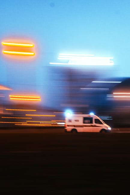 A white van parked on a pavement during dusk, with blurred city lights and illuminated signs in the background creating a streaked light effect due to motion blur. The scene suggests urban surroundings and may be part of a home relocation or furniture transport process, coordinated by a removal service such as Man with Van Shooters Hill, with the focus on vehicle positioning and environmental lighting for house removals or emergency moves.